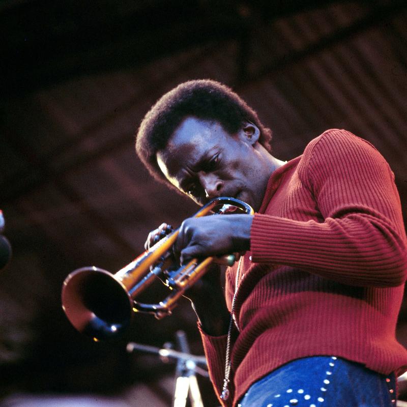 Jazz legend Miles Davis playing the trumpet in a red shirt